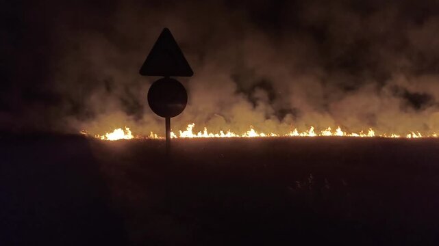Fuego forestal en la noche junto a carretera con tr&aacute;fico 