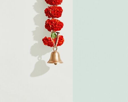 Small brass bell with a vibrant marigold garland and iron nail, featuring brushed metal and floral textures for festival supply and doorway decoration, with copy space