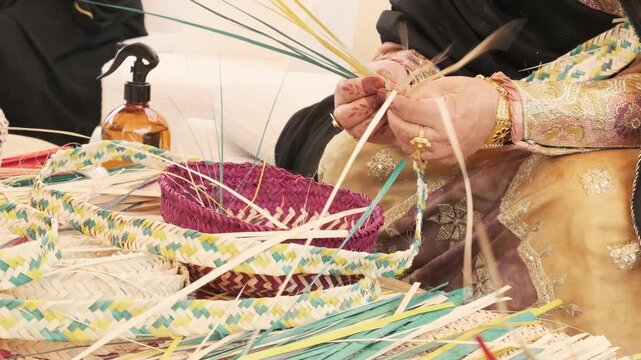 Palm frond weaving by Emirati hands creates basket forms and tray with colored strips. Gold sleeves and jewelry frame careful motions that reflect Arabic craft heritage and Bedouin tradition.