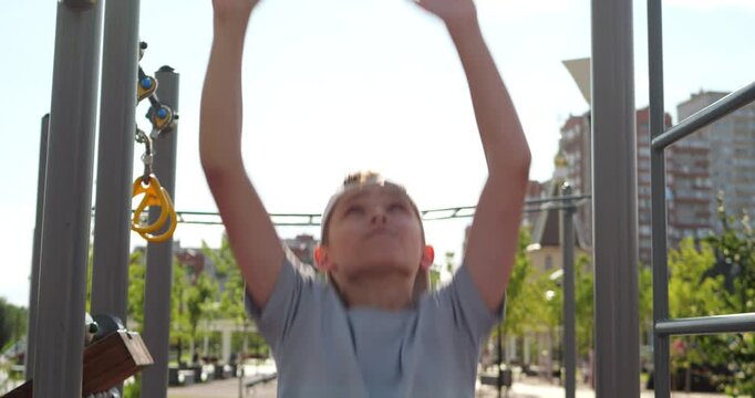 Teenager prepares for pull-ups at outdoor sports ground, turns cap backward, rubs hands and jumps to horizontal bar. Dynamic workout captures focus, strength and determination