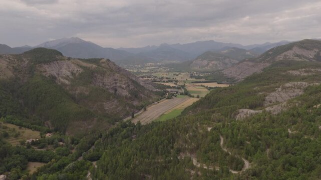 Wide aerial of green valley agricultural fields gray eroded slopes and distant mountain ranges under cloudy sky