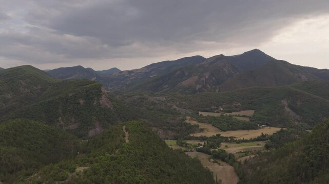 Expansive aerial of green forested hills open fields scattered farms and layered mountain ridges under heavy clouds