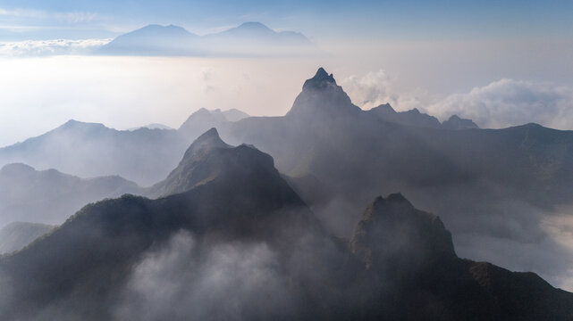 Aerial view of the volcanic peaks of Gunung Kelud rising above a sea of clouds with dramatic mist and soft morning light in Kecamatan Ngancar, Jawa Timur, Indonesia.