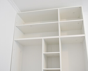 Low angle view of a large white modular shelving unit installed against a clean white wall in a bright modern room, showcasing its spacious compartments, empty shelves, and minimalist interior design © Gulmira Uatkhanova