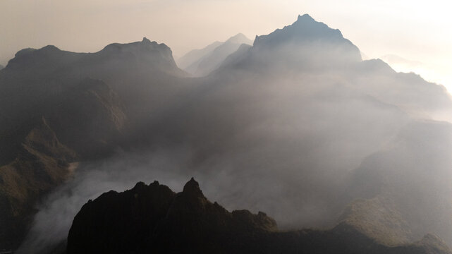 Aerial view of Gunung Kelud featuring rugged volcanic peaks shrouded in thick mist and soft morning light, Kecamatan Ngancar, Jawa Timur, Indonesia.