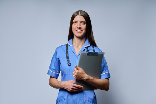 Smiling female nurse holding clipboard with patient records standing against grey background