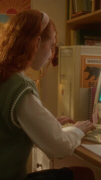 Vertical video of Caucasian teenage girl typing on vintage computer keyboard in retro room. Footage is perfect for nostalgia marketing or educational history videos