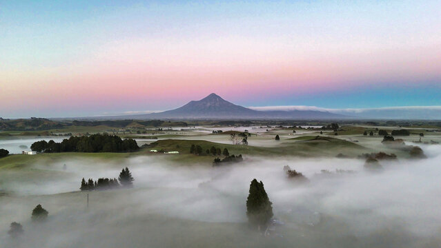 Aerial view of Mount Taranaki rising above the morning mist covering the rolling green hills and Lake Ratapiko, Ratapiko, Taranaki Region, New Zealand.