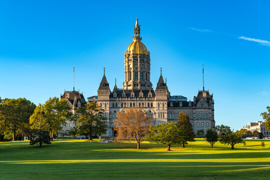 The historic Connecticut State Capitol building with its bright gold dome sits on the expansive green lawn of Bushnell Park in Hartford, Connecticut.