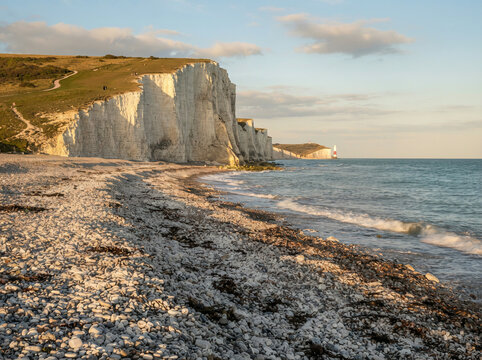 Dramatic white chalk cliffs and rocky shoreline with grassy cliff path and distant red and white