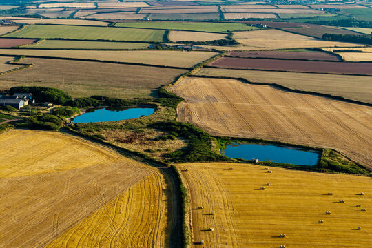 Aerial view of farmland and irrigation ponds in coastal Pembrokeshire, Wales, evening light over harvested stubble fields bordered by hedgerows