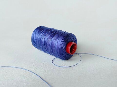 blue sewing thread spool on white background with loose thread