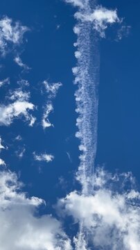 Cumulus clouds against a blue sky, with a dynamic contrail from an airplane. Vertical view, travel background, and peaceful atmosphere