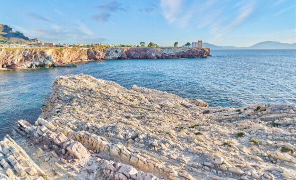 Scenic Mediterranean coastline of Sicily, Italy, with rugged rocks in the foreground, clear blue sea, distant mountains and cliffs under beautiful sunny summer weather.