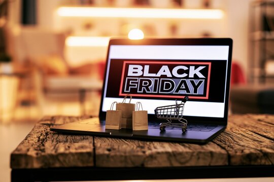Laptop displaying a black friday sale with a miniature shopping cart and paper bags
