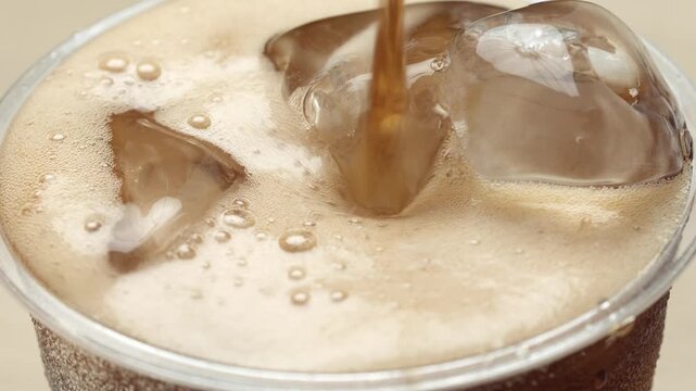 Slow motion soft drink pouring with ice cubes and bubbles.