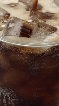 Slow motion soft drink vertical pouring with ice cubes and bubbles, 