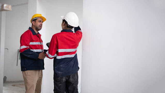 Construction engineers inspecting interior walls inside an unfinished building while reviewing structural conditions with a digital tablet. Building inspection, teamwork, workplace safety, renovation.