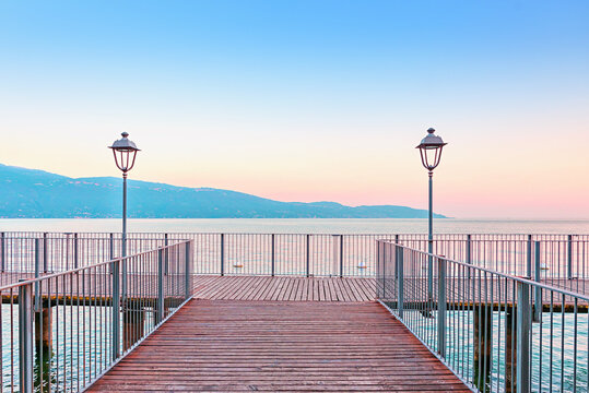 Wooden walkway with a railing and two lanterns. Lake Garda shoreline Gargnano, italy