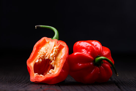Red habanero peppers with cut half showing seeds on wooden surface. Fresh chili pods interior detail rustic background
