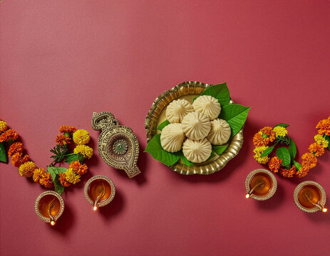 Traditional Diwali Arrangement With Modak Sweets, Brass Plate, Marigold Garlands and Lit Oil Lamps