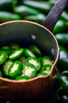 Close view of metal pot with jalapeno slices on dark background. Fresh green chili preparation detail