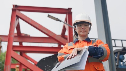 Fototapeta premium Asian female technician in hardhat checking factory wastewater treatment facility and drainage basin with clipboard. Industrial water management, ESG environmental sustainability concept.