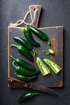 Black jalapeno with knife on rustic wooden cutting board close up. Green mexican jalapeno hot peppers