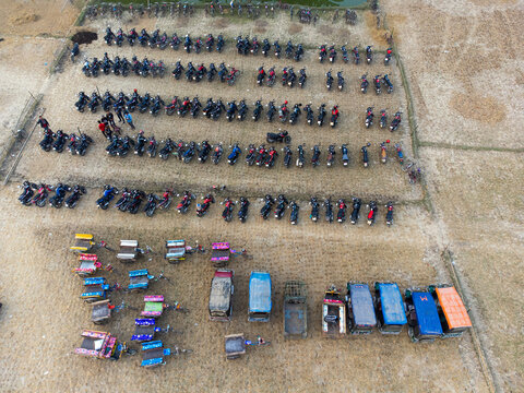 Aerial view of a large parking area filled with numerous motorcycles arranged in rows alongside small three-wheeled vehicles on a dry, dusty field in Rajshahi, Rajshahi Division, Bangladesh.