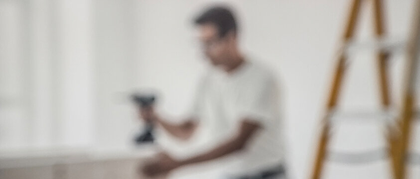 A blurred image of a person using a power tool in a bright and minimalistic interior space, conveying the theme of home improvement and DIY projects.