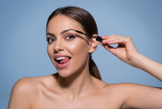Playful woman applying brow gel or mascara looking at camera