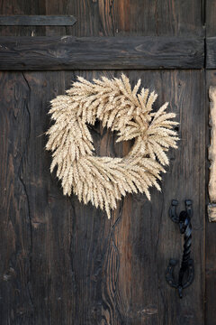 Rustic wreath made golden wheat stalks hanging on old wooden door of country house, traditional harvest decoration and autumn farmhouse decor.