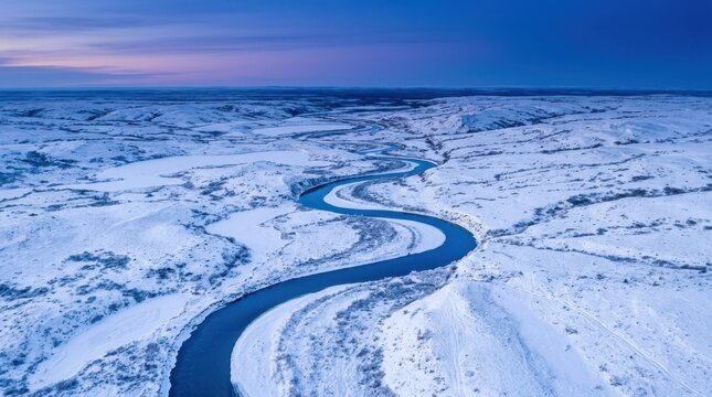 Beautiful winter landscape background. Dark blue river winding gracefully through a vast flat expanse of snow covered tundra landscape.