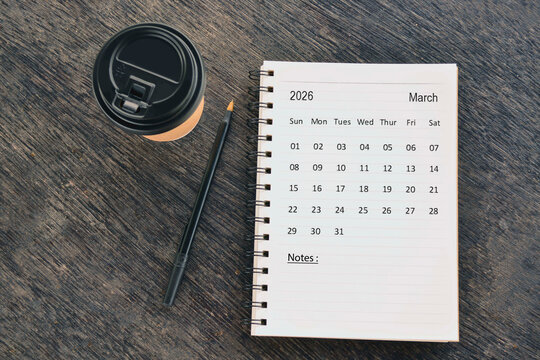 March 2026 desk calendar with disposable coffee cup and pen on wooden table. Directly above. Flat lay.