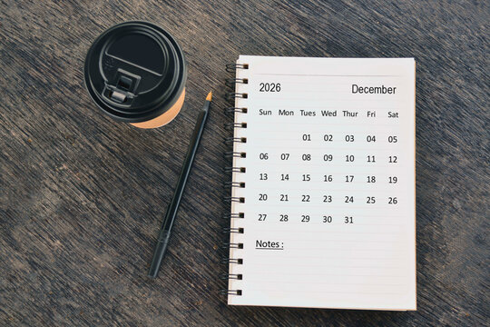 December 2026 desk calendar with disposable coffee cup and pen on wooden table. Directly above. Flat lay.