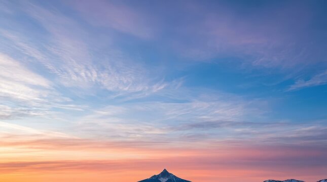 Stunning winter landscape background. A distant mountain peak is silhouetted against a vast expansive sky filled with soft colorful twilight clouds.