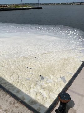 River foam on the Southern Bug River in Mykolaiv Ukraine, waves pushing white foam toward a port, close view of turbulent water surface, natural river phenomenon and industrial waterfront scene