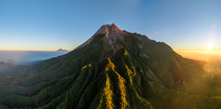 Aerial view of Mount Merapi with lush green slopes, volcanic terrain, and golden sunrise light in Cangkringan, Special Region of Yogyakarta, Indonesia.