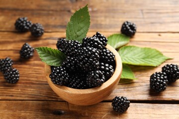 Ripe blackberries in bowl with leaves on wooden table, closeup © New Africa