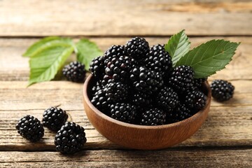 Ripe blackberries in bowl with leaves on wooden table, closeup © New Africa