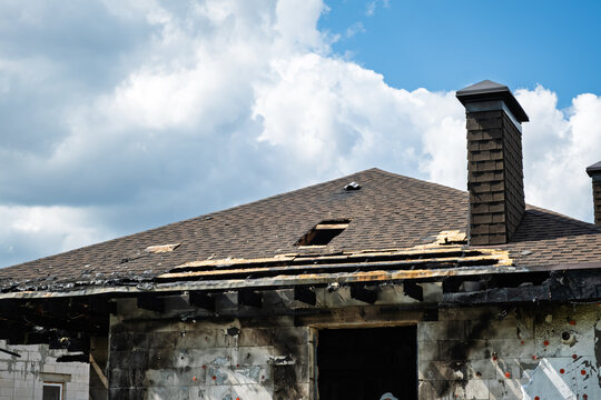 Damaged brick chimney stands on the roof of burned house. Concept of fire insurance. Arson case. Consequences of a gas or battery explosion. Home maintenance, structural repair, building inspection.