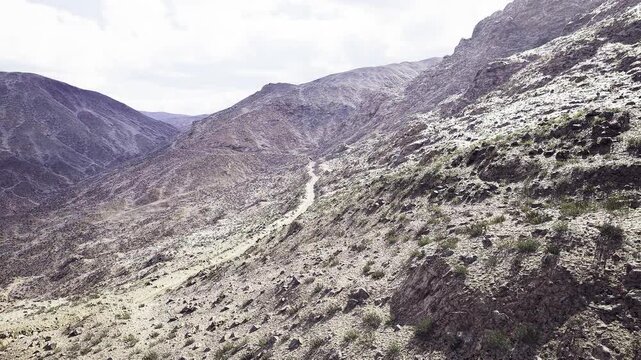 Aerial arid mountain path winding through scrubby hills, drone perspective capturing muted tones and solitary valley, ideal for remote trekking, route planning