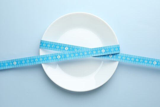 Anorexia. Empty plate and measuring tape on light blue background, top view