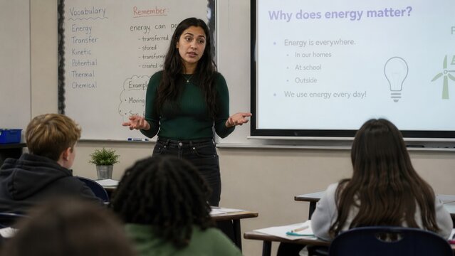 Female science teacher explaining energy concepts during classroom lesson with students and presentation screen