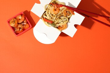 Naklejka premium Delicious wok with shrimps in takeaway box on orange background, top view. Space for text