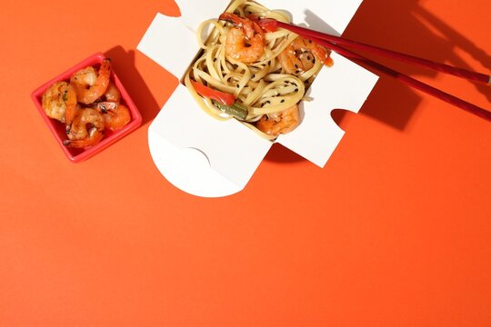 Delicious wok with shrimps in takeaway box on orange background, top view. Space for text