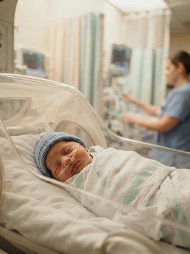 Swaddled newborn with a nasal cannula as a nurse tends equipment nearby