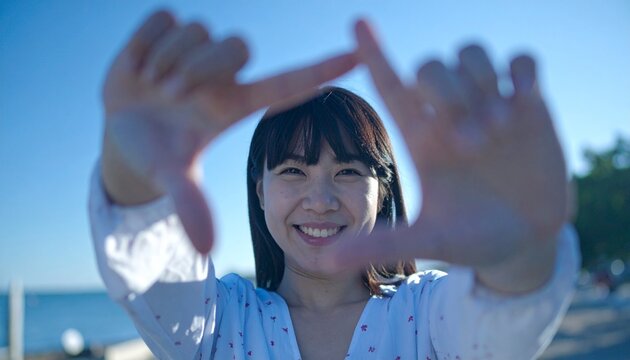 親しみやすい表情で、両手を使って顔の前で長方形のフレームを作る