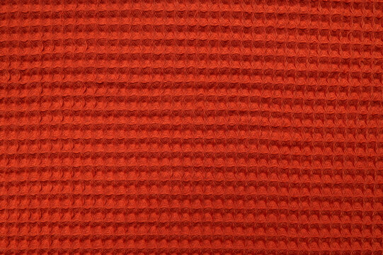 Waffle texture of towel or blanket close-up. Fabric background, wallpaper. Vibrant red and orange colors of cotton material, cozy autumn abstract background. Textile detail, cloth pattern