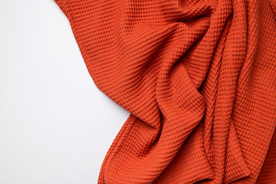 Bright orange waffle fabric drapes over light gray background, showing cotton texture and open space for text. Textile styling, soft folds, and warm color suit autumn branding and decor.